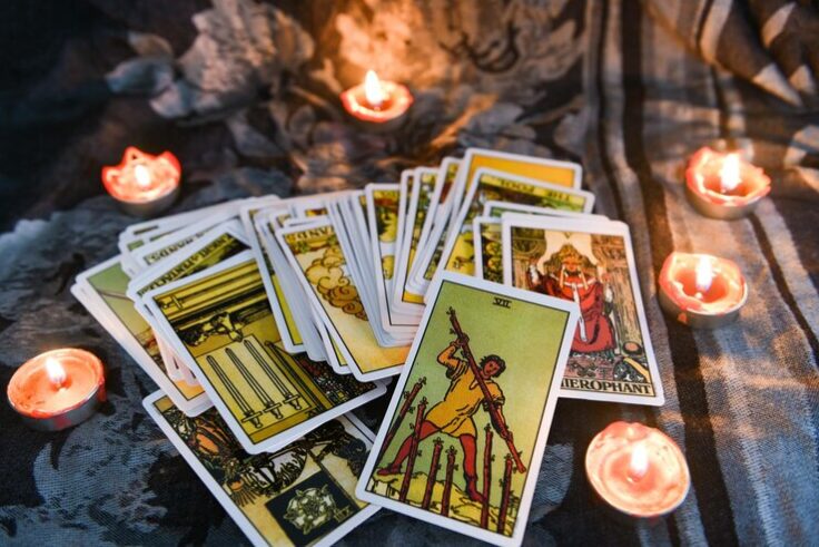 Mazo de cartas de tarot puestas en una superficie oscura, rodeada de 6 velas encendidas.